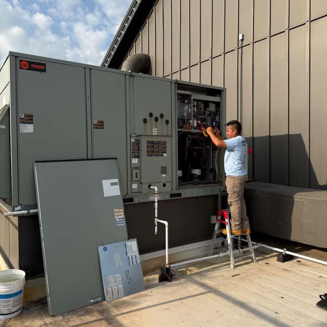 Technician on a ladder working inside the control panel of a rooftop package unit