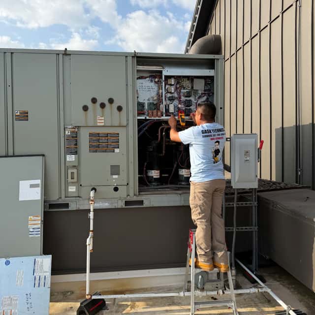 Technician metering the control panel of a rooftop package unit