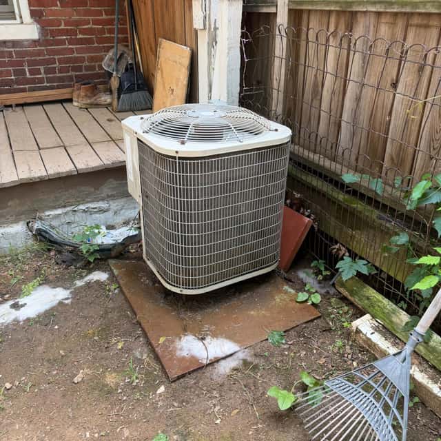 Residential condenser on a pad beside a wooden fence after cleaning