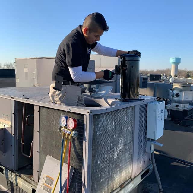 Technician charging a rooftop package unit with a gauge set
