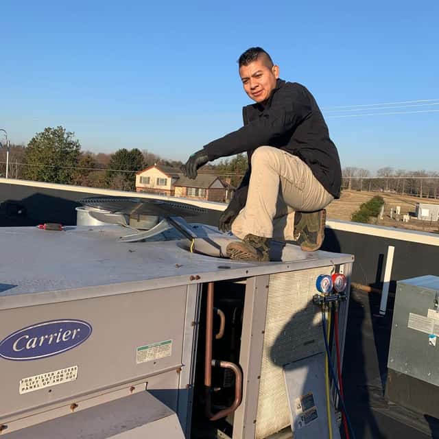 Technician kneeling on a Carrier rooftop unit, taking readings